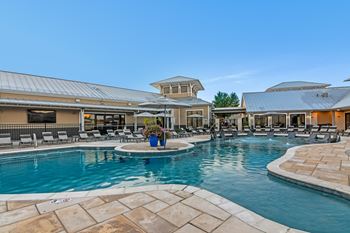 A large outdoor swimming pool surrounded by a stone patio and lounge chairs at Crossgates Apartment Homes, Starkville